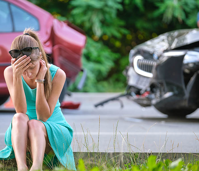 Woman sitting on side of the road following fender bender car accident